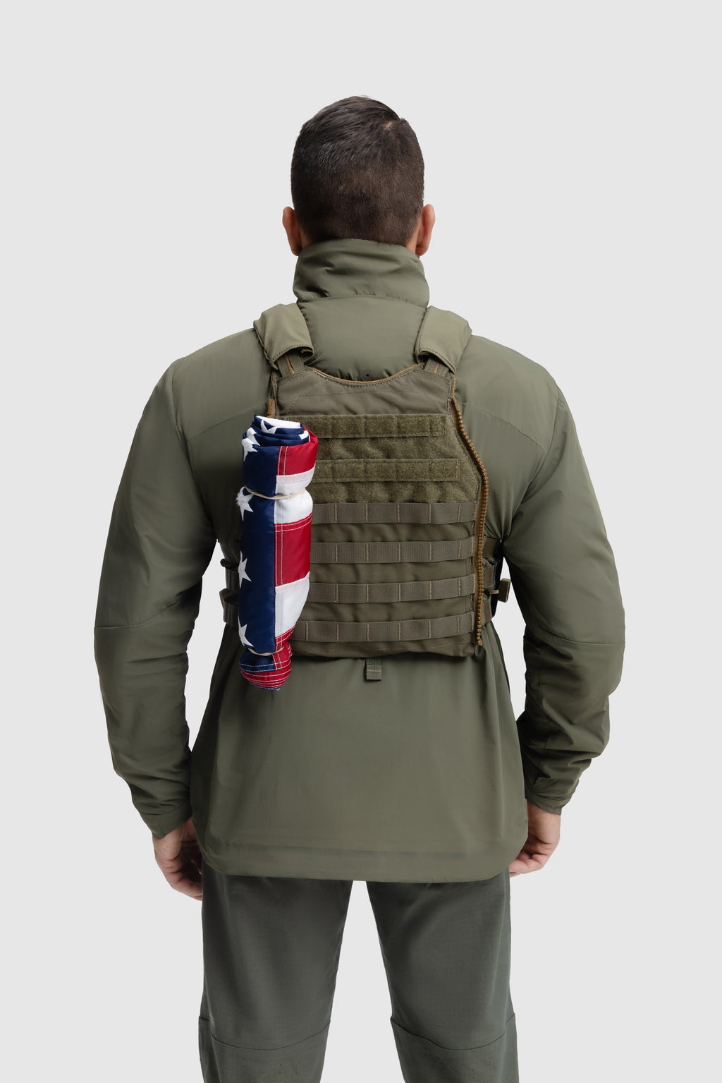Back photo of the Tomahawk Performance Crosswind Jacket, a tactical windbreaker, worn under a carrier in Ranger Green color way.