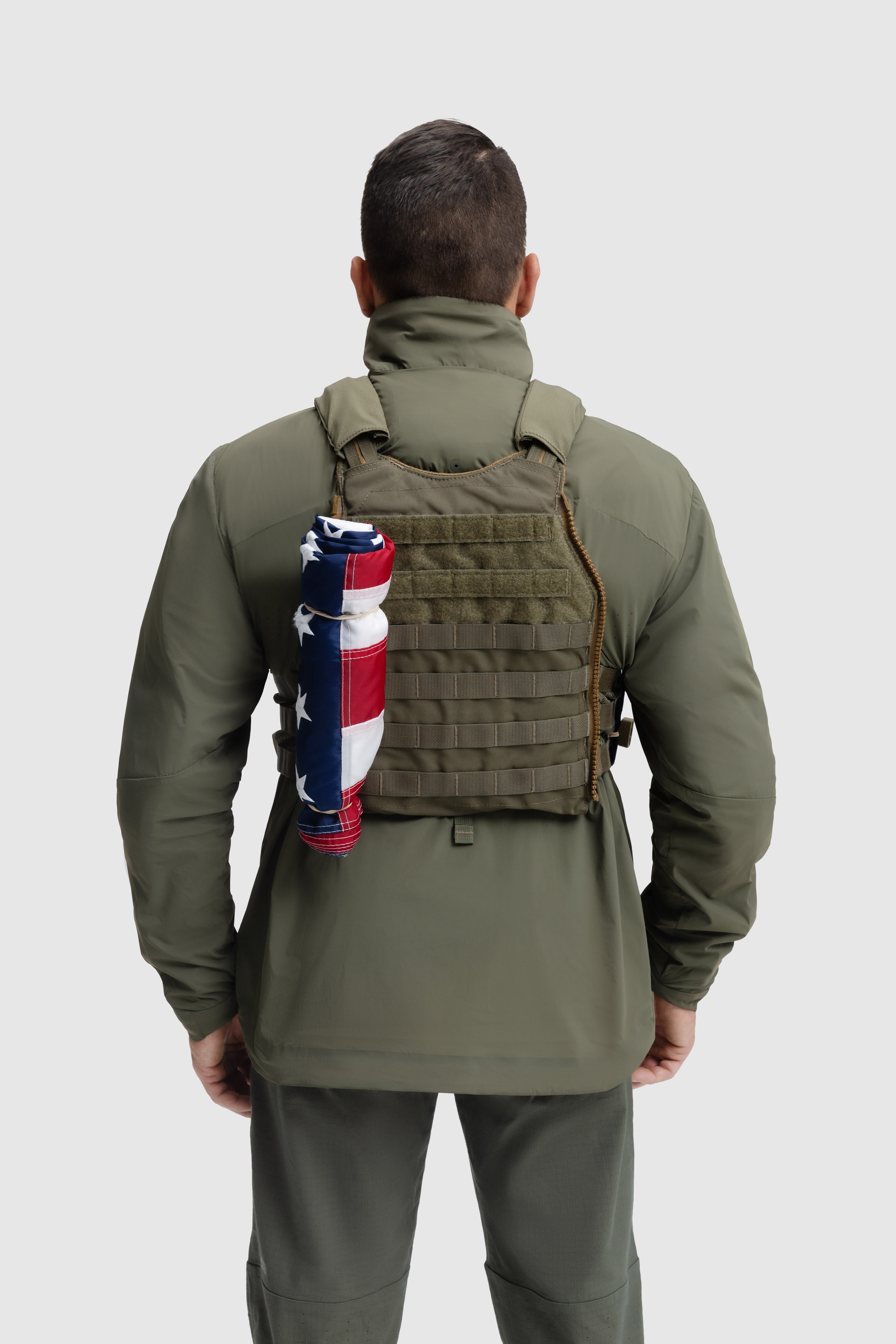 Back photo of the Tomahawk Performance Crosswind Jacket, a tactical windbreaker, worn under a carrier in Ranger Green color way.