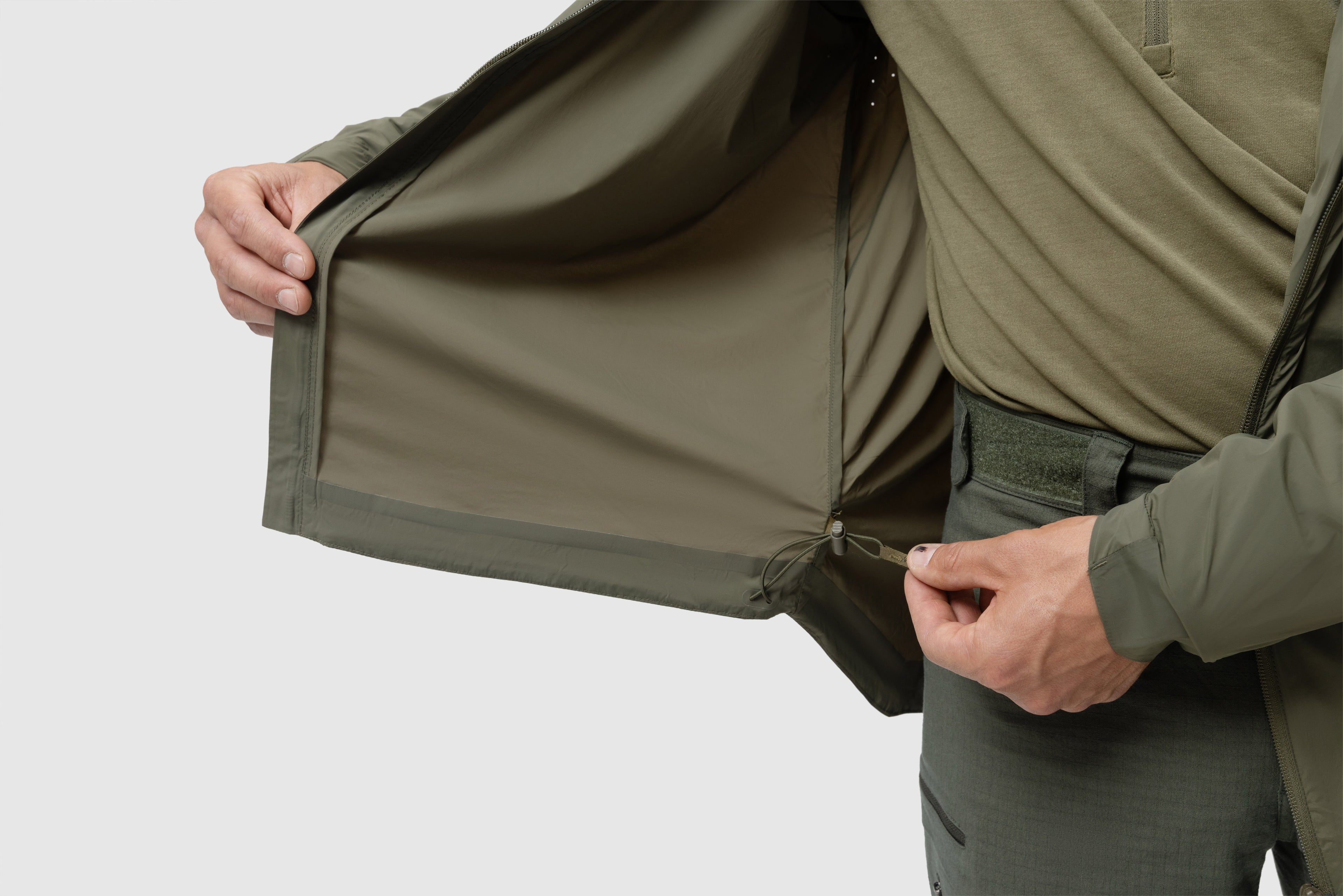 Photo of the Tomahawk Performance Crosswind Jacket's interior lining around the hem including adjustable hem drawstring in Ranger Green color way. Laser perforation for ventilation also shown.
