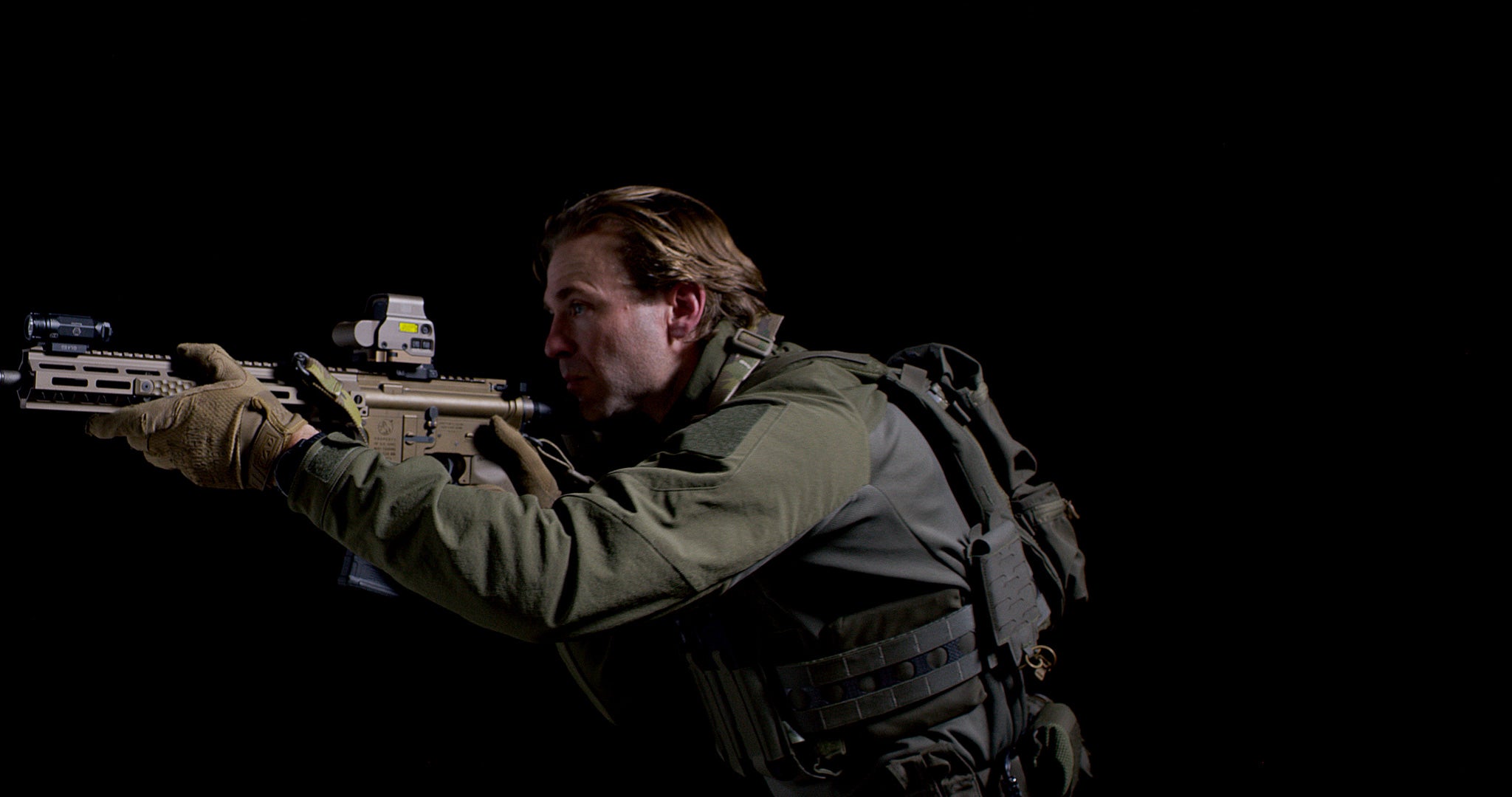 Person in tactical gear (the Tomahawk Performance CW / Combat Top) holding a rifle against a dark background