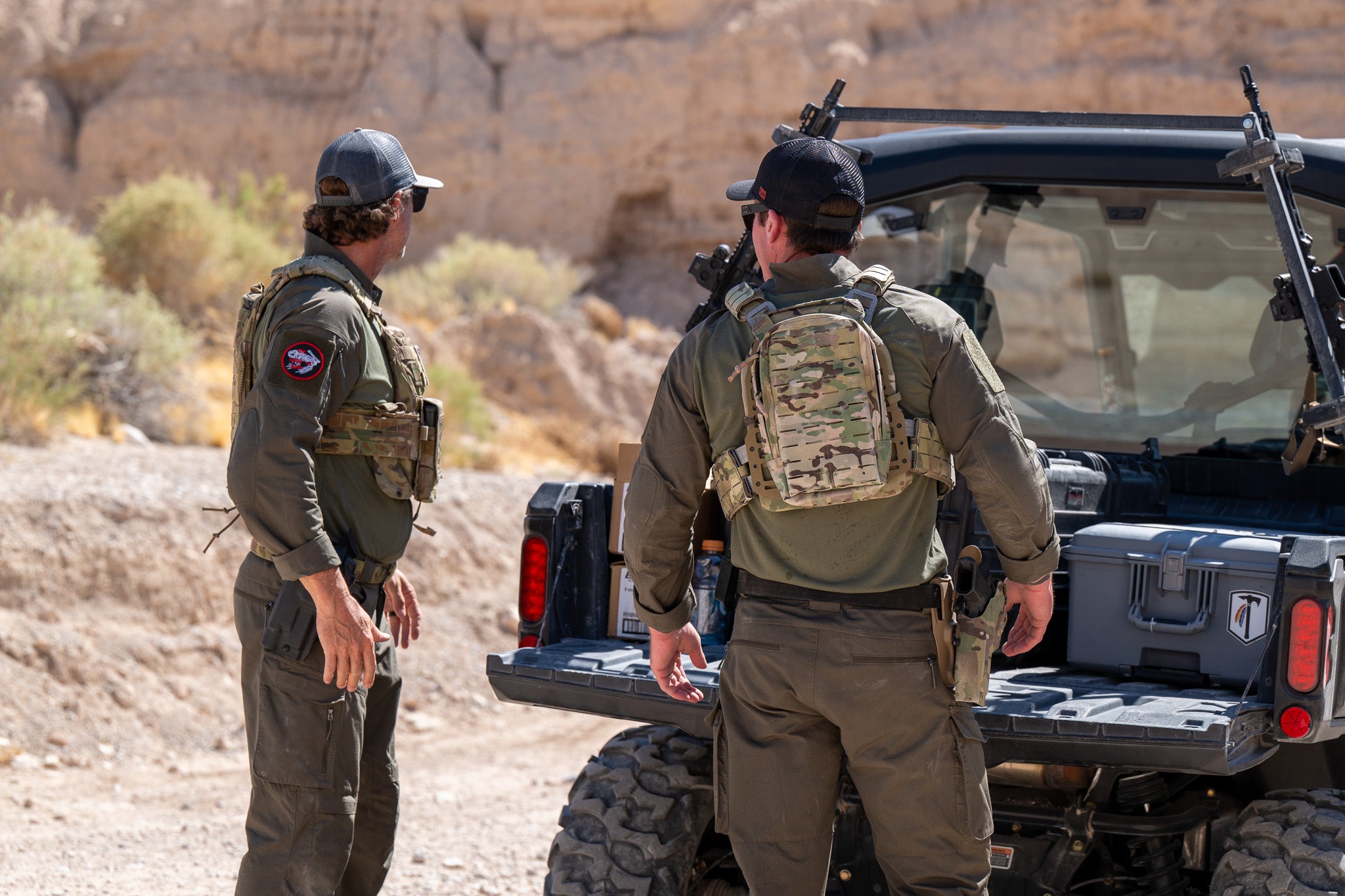 Two men wearing the Tomahawk Performance HW / Combat Uniform loading gear out of a side-by-side vehicle.